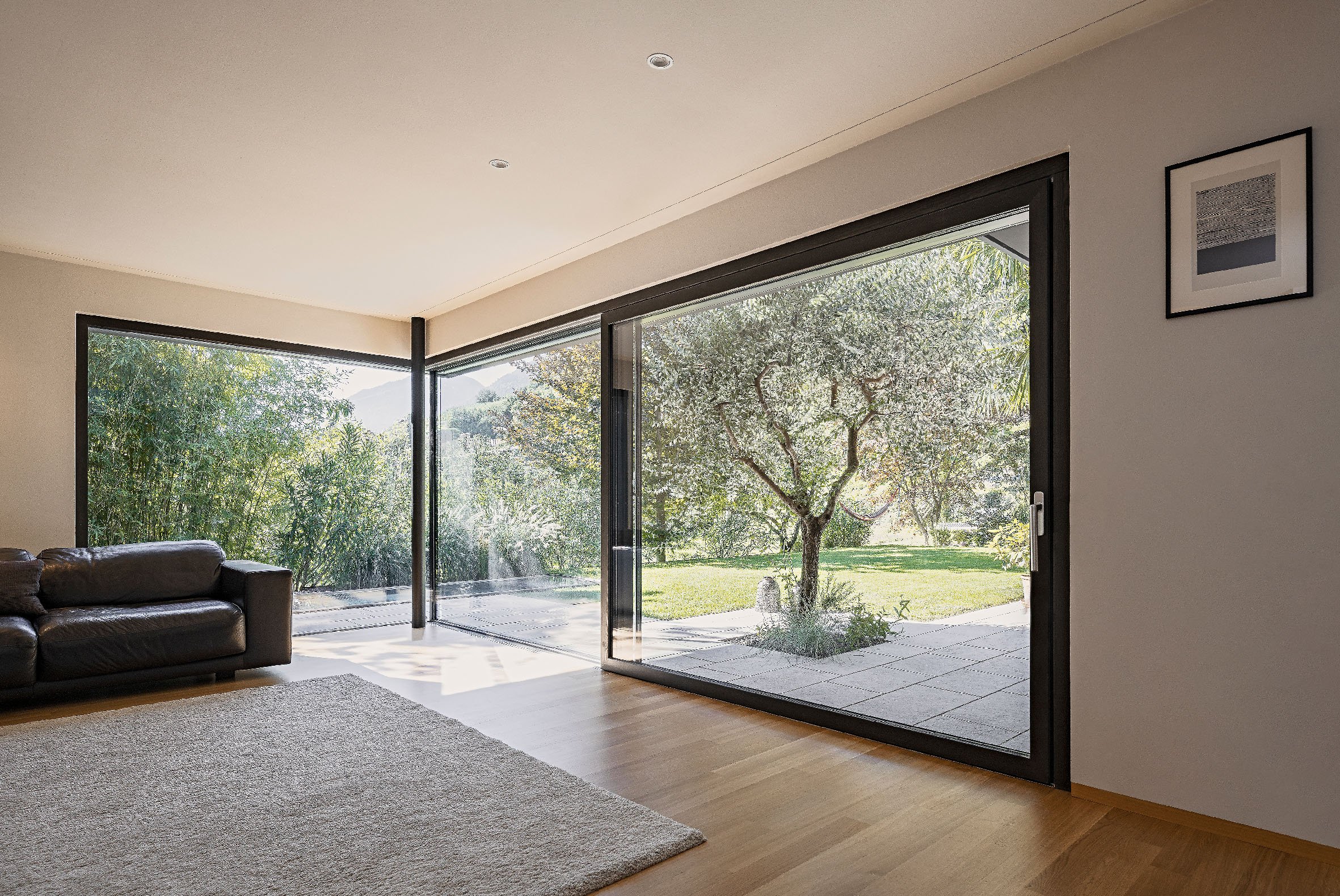 Moderner, heller Wohnraum mit raumhohen Panoramafenstern in schwarzem Rahmen.